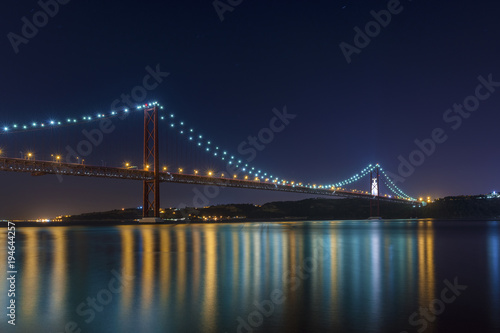 Beautiful and serene view of the Tagus River and the 25 of April Bridge (Ponte 25 de Abril) at night, in Lisbon, Portugal; Concept for visit Lisbon