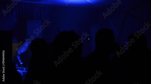 People raising their hands in front of bright stage lights. Young people dancing and listening music at concert. Fans raising their hands at festival. Silhouettes of concert crowd. Nightlife in club photo