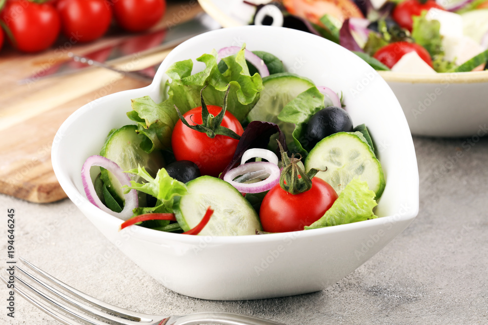 bowl of salad with vegetables and greens, with tomato, cucumber and onions.