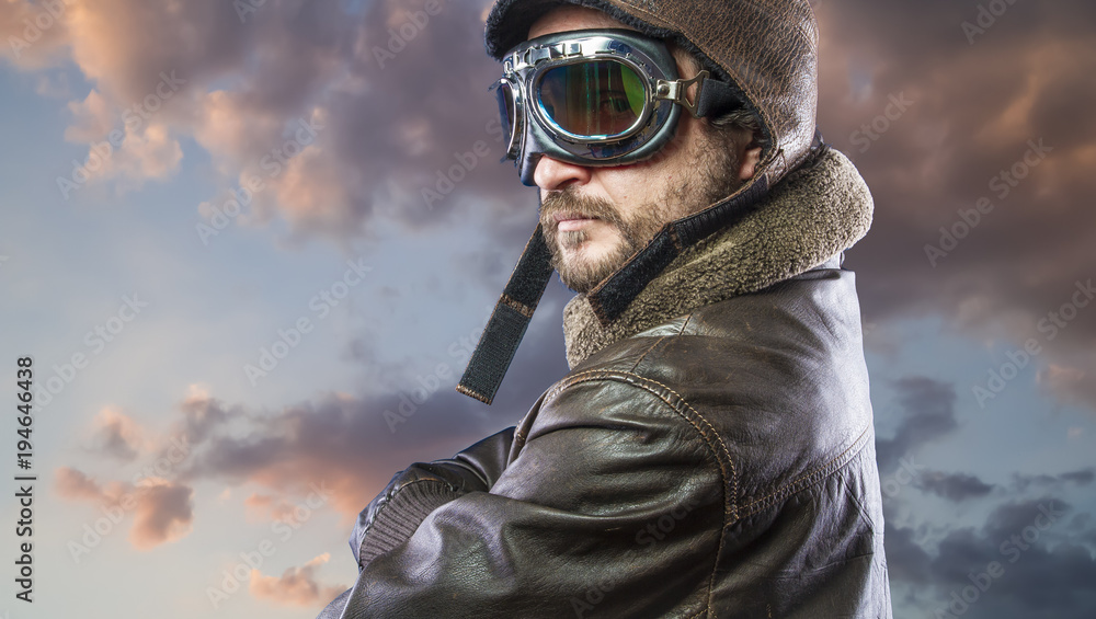 Fototapeta premium Proud, pilot of the 20s with sunglasses and vintage aviator helmet. Wears leather jacket, beard and expressive faces