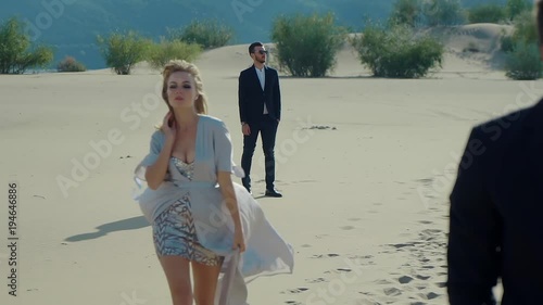 Attractive woman is torning between two men. She is walking from one to second over sunny river shore in summer day