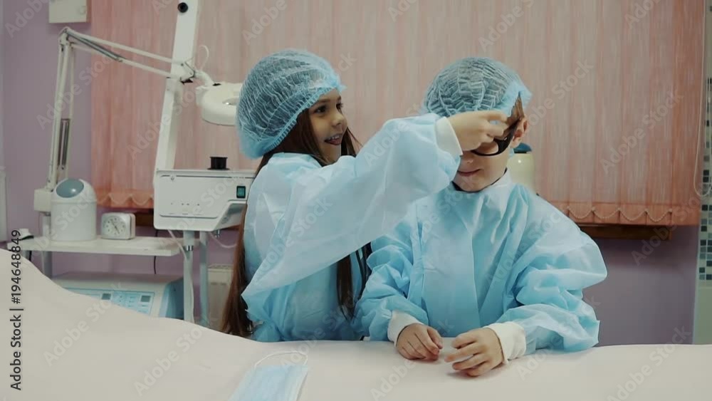 Children are playing in a clinic cabinet like doctors. Girl is putting on boys head a protective medical hat Children are playing in a clinic cabinet like doctors. Girl is putting on boys head a protective medical hat