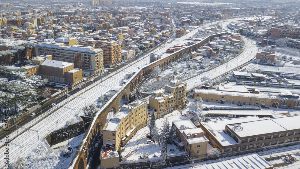 Aerial view of the Tuscolana station in Rome, Italy. Around the tracks there are the palaces and streets of the Italian city. The railroad tracks are made of steel. Everything is covered by snow