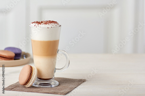 Tableau sur toile Glass cup of coffee latte and colorful macaroons on wooden table