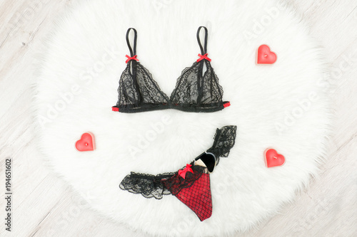 Fashion concept. Black lacy bra and panties on white fur. Red heartshaped candles