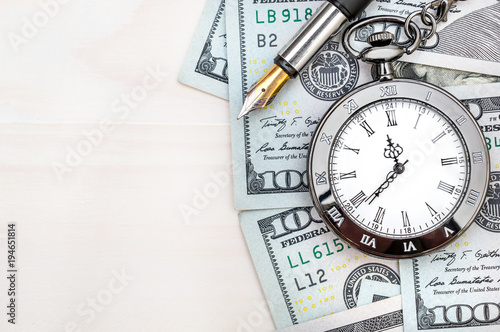 Pocket watch with dollar bills and pen on white wooden background. Business background.