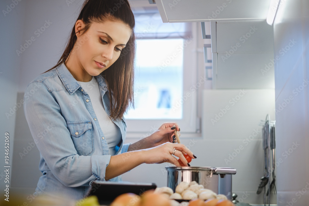 Girl cooking and looking recipe on tablet screen