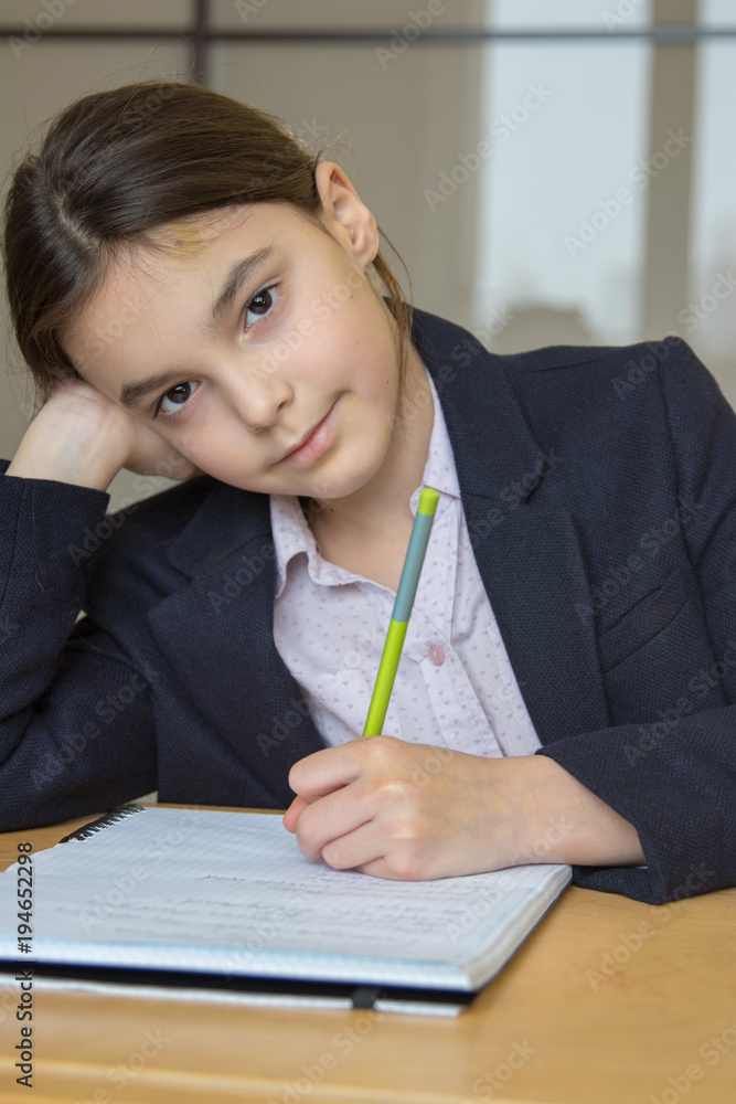 girl writes in a notebook sitting at a wooden table