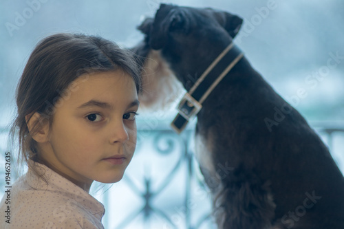 beautiful little girl is sitting on a window sill with her favorite dog