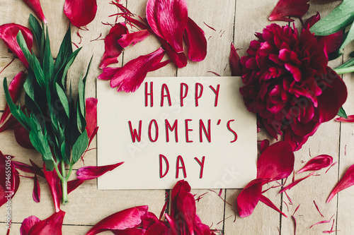 happy women's day text sign on craft card and beautiful red peonies on wooden rustic background, flat lay. modern greeting card. womens day
