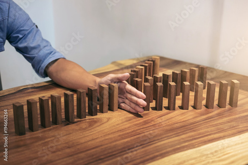 Risk and strategy in business, Close up of businessman hand stopping wooden block between three way from falling in the line of domino