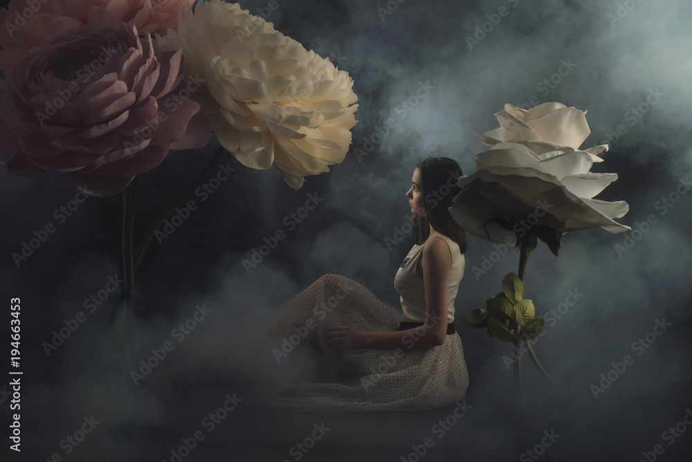 girl in a light dress among the huge flowers made of paper and formina