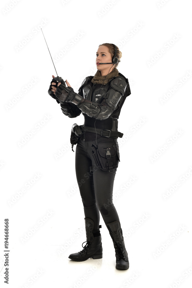 full length portrait of female soldier wearing black tactical armour, holding a remote control, isolated on white studio background. full length portrait of female soldier wearing black tactical armour, holding a remote control, isolated on white studio background.
