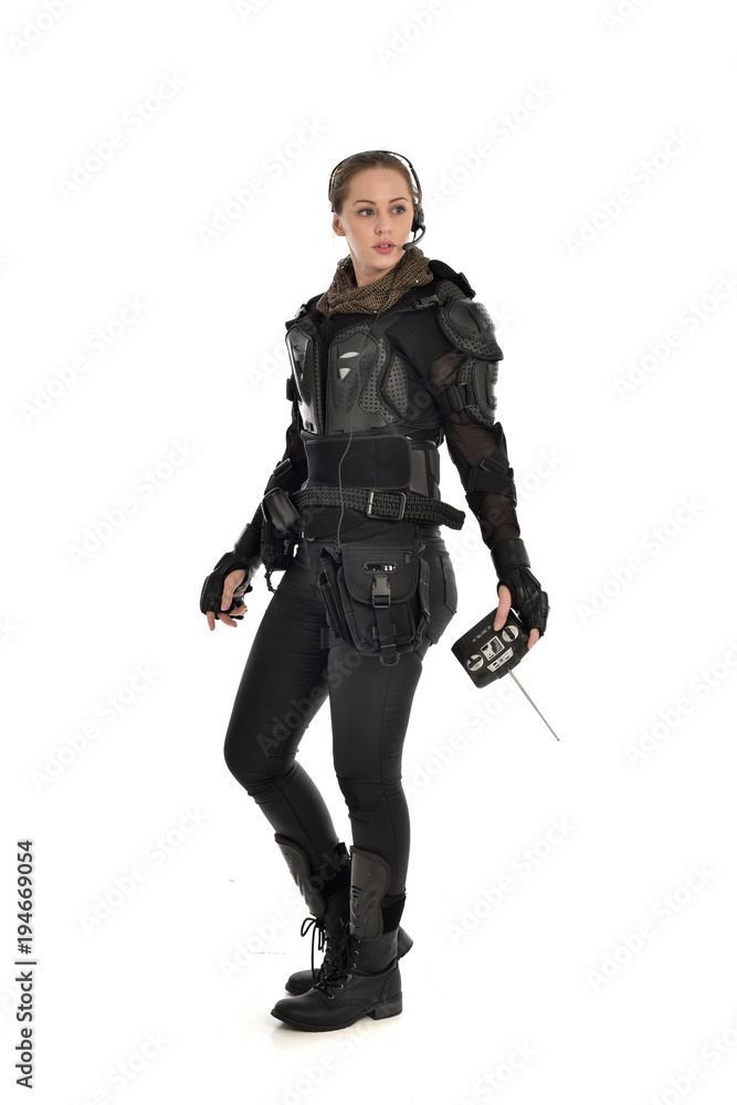 full length portrait of female soldier wearing black tactical armour, holding a remote control, isolated on white studio background. full length portrait of female soldier wearing black tactical armour, holding a remote control, isolated on white studio background.