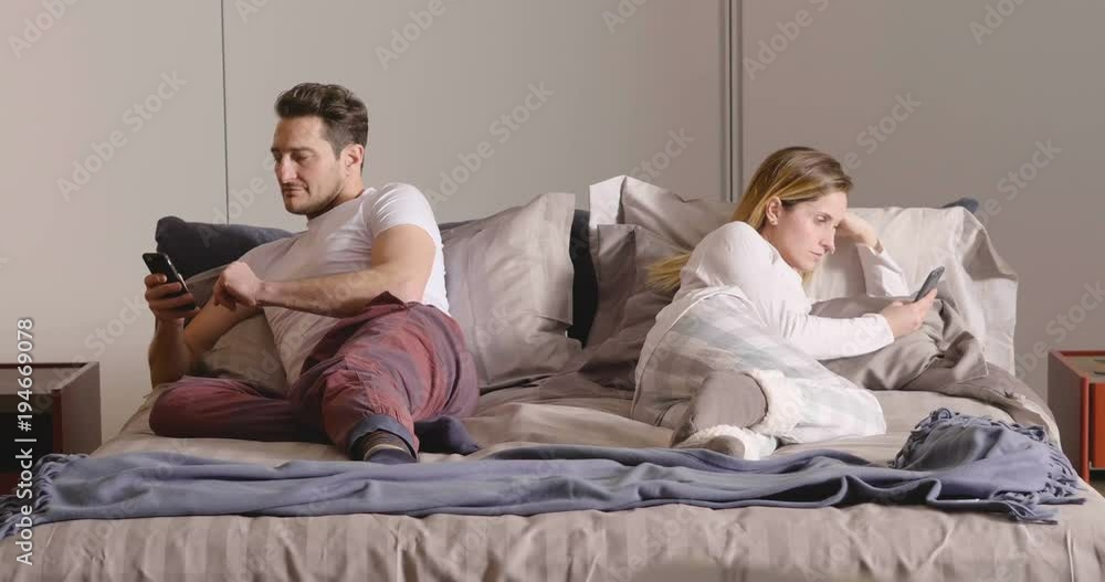 A married couple in bed use the phone separately to send messages or use social networks and no longer talk to each other. Concept of: new generations, separation, technology. A married couple in bed use the phone separately to send messages or use social networks and no longer talk to each other. Concept of: new generations, separation, technology.