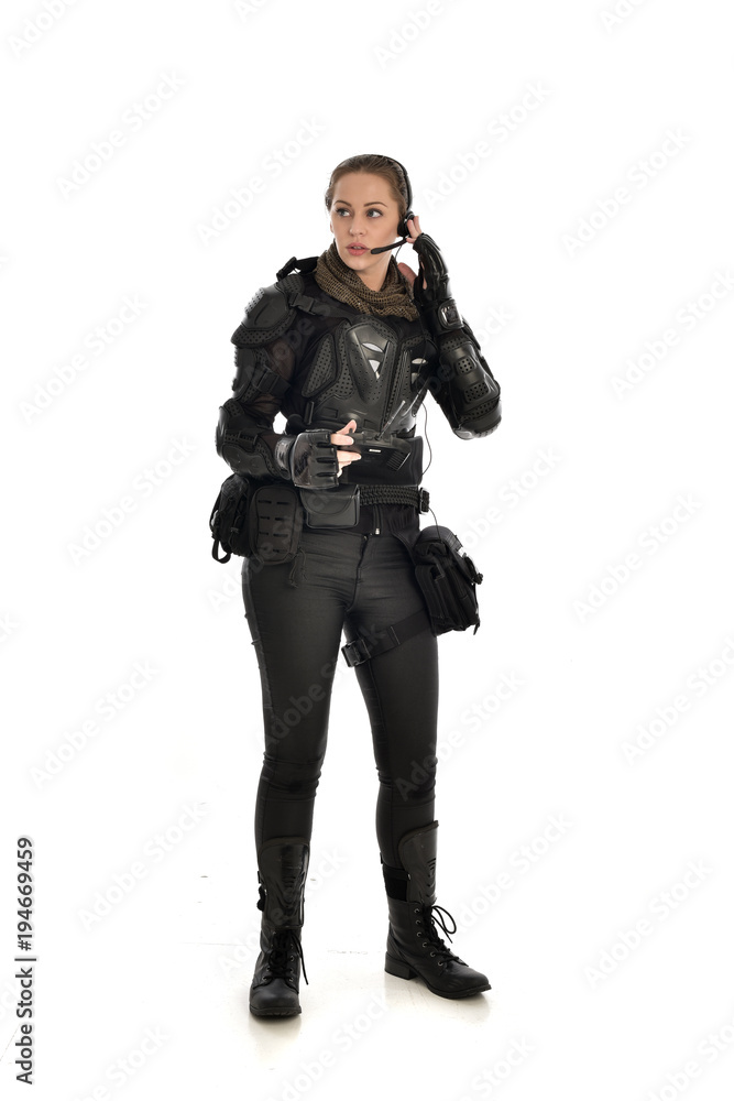 full length portrait of female  soldier wearing black  tactical armour, holding a remote control, isolated on white studio background.