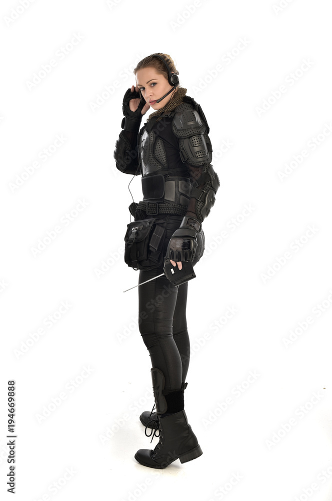 full length portrait of female  soldier wearing black  tactical armour, holding a remote control, isolated on white studio background.