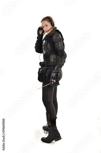 full length portrait of female soldier wearing black tactical armour, holding a remote control, isolated on white studio background.