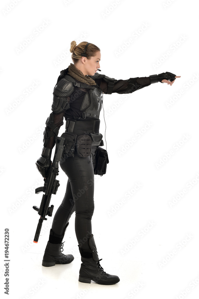 full length portrait of female  soldier wearing black  tactical armour, holding a rifle gun, isolated on white studio background.