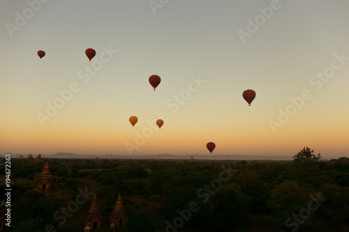 Hot air balloons floating around Burmese pagoda heritage site during sunrise landscape.