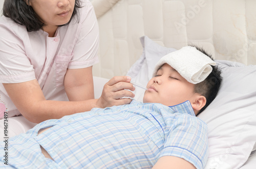 Mother measuring temperature of her ill kid. Sick child with high fever laying in bed and mother holding thermometer, Healthy care concept