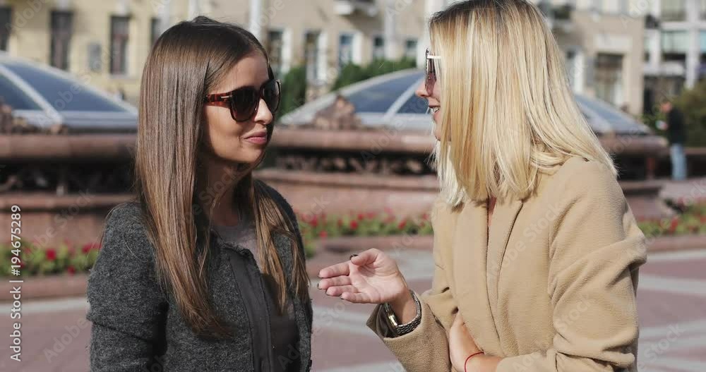 Blonde and brunette girlfriends talking in a city on the urban background. Blonde and brunette girlfriends talking in a city on the urban background.