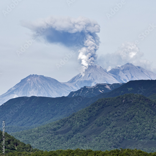 Scenery summer mountain landscape of Kamchatka Peninsula: explosive-effusive eruption of Zhupanovsky Volcano powerful plume of gas, steam, ash from crater active volcano, mountains with green forest