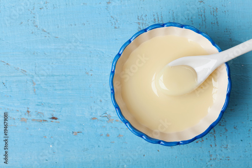 Condensed milk or evaporated milk in bowl on blue table top view.