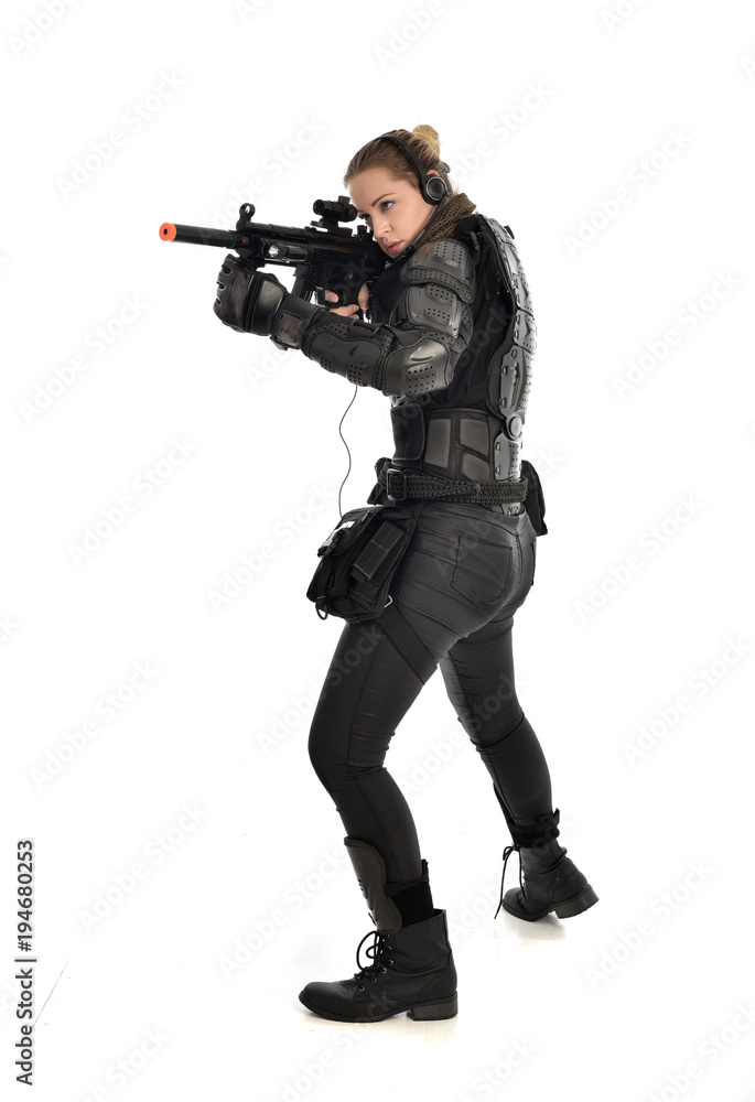 full length portrait of female  soldier wearing black  tactical armour, holding a rifle gun, isolated on white studio background.