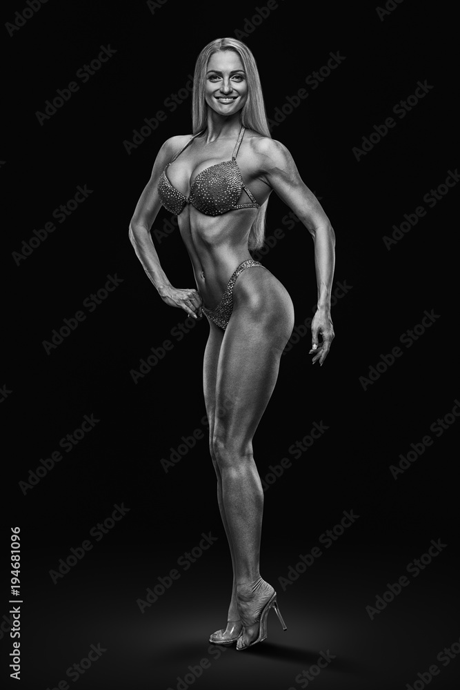 Black and white image inspire concept champion female fitness bikini model competition Confident attractive happy young bodybuilder looking forward Sports slim body perfect shape Black background