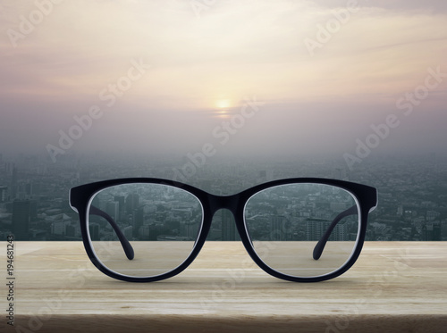 Black eye glasses on wooden table over city tower at sunset, vintage style, Business vision concept