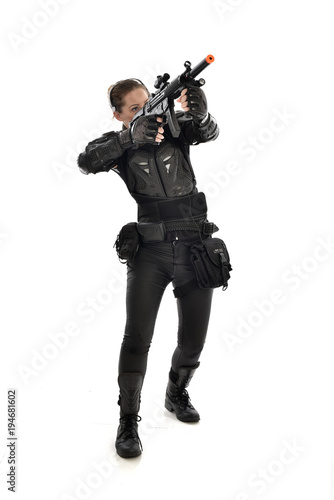 full length portrait of female soldier wearing black tactical armour, holding a rifle gun, isolated on white studio background.