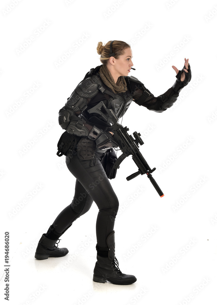 full length portrait of female soldier wearing black tactical armour, holding a rifle gun, isolated on white studio background. full length portrait of female soldier wearing black tactical armour, holding a rifle gun, isolated on white studio background.
