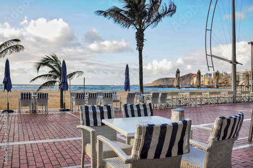 Passage at the urban beach of Las Palmas. Las Canteras. Empty tables with no tourists on cold but sunny day. Sea view and few clouds on the horizon HDR
