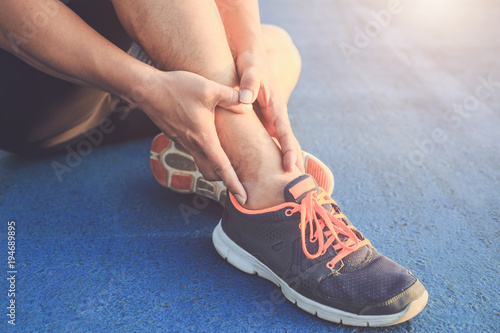 Injury from workout concept   Asian man use hands hold on his ankle while running on road in the park. Focus on ankle.