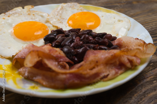 Plate with scrambled eggs, bacon and beans on a wooden rustic table.