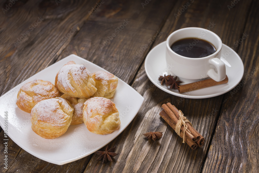 Delicious eclairs sprinkled with icing sugar, stand on a wooden table. Copy spase. Delicious eclairs sprinkled with icing sugar, stand on a wooden table. Copy spase.