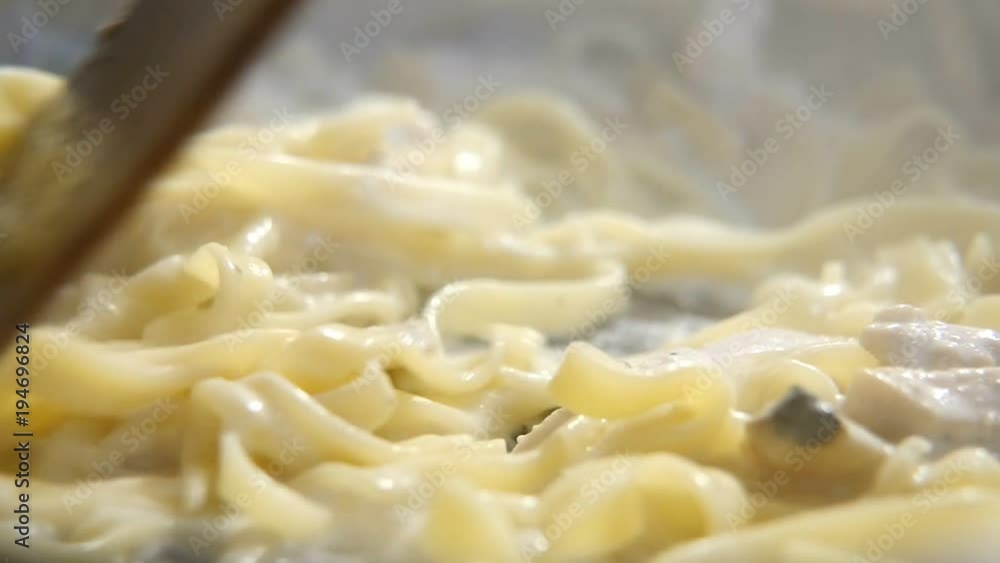 An exciting closeup of a wooden spatula mixing macaroni and mushrooms in a metallic pan. The pan is full of dense vapour. The meal looks wonderful An exciting closeup of a wooden spatula mixing macaroni and mushrooms in a metallic pan. The pan is full of dense vapour. The meal looks wonderful