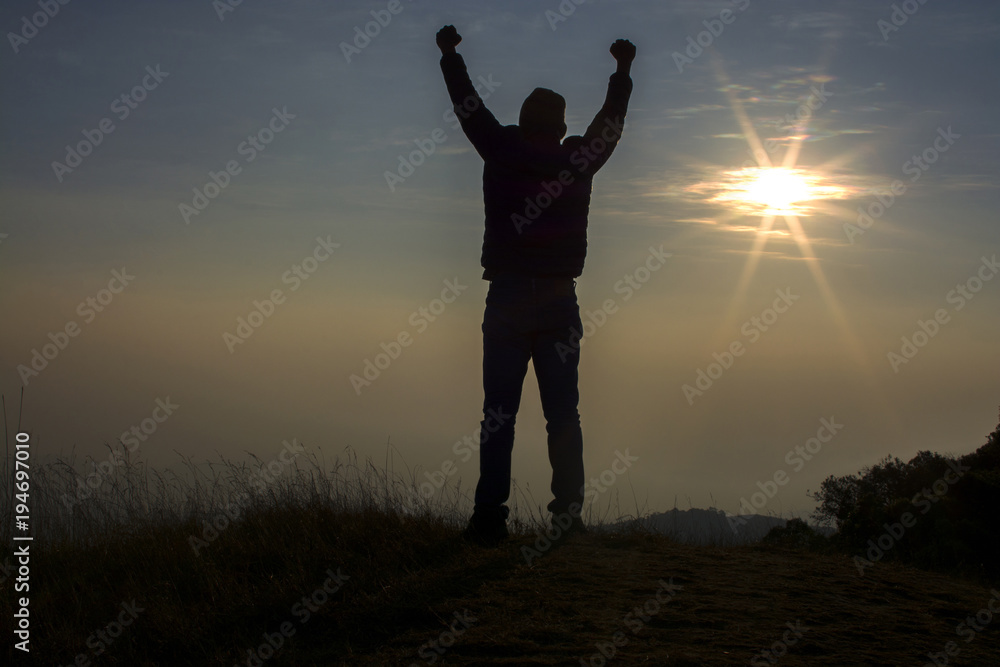 Man putting his hands up and standing on cliff at sunset time