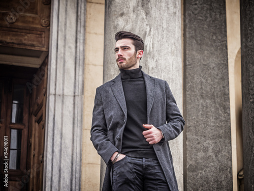 Handsome bearded young man outdoor in winter fashion, wearing black turtleneck sweater and woolen blazer jacket in city setting