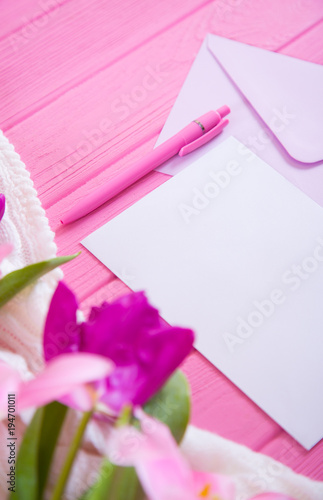 Clear sheet of white paper with pen and envelope and tender bouquet of beautiful tulips on pink wooden background