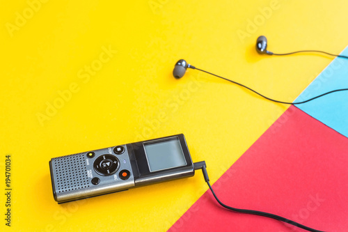 Black voice recorder with headphones on a combined yellow, blue and red background. Journalism concept. Equipment for work, interview and voice recording. Top view. Flat lay. Copyspace