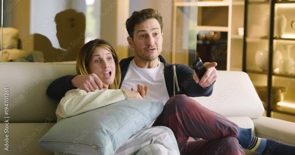 A couple of lovers watch television embraced on the sofa in the new house and watch a movie together. Concept of: leisure, relax, tv. A couple of lovers watch television embraced on the sofa in the new house and watch a movie together. Concept of: leisure, relax, tv.
