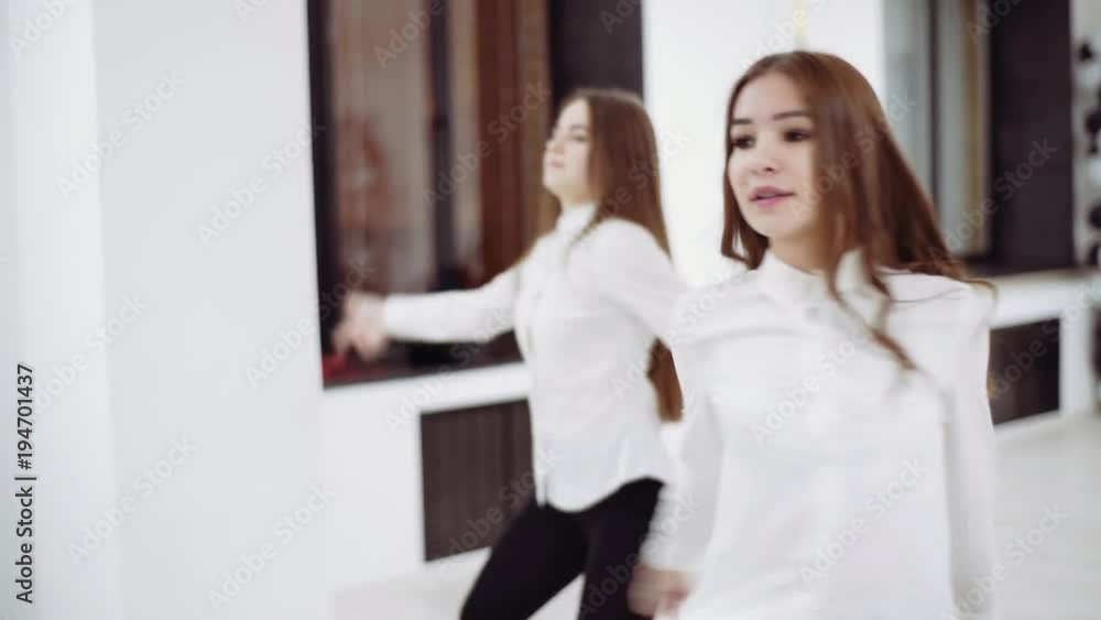 Two girls in white blouses and black trousers dance in front of the mirror. Two girls in white blouses and black trousers dance in front of the mirror.