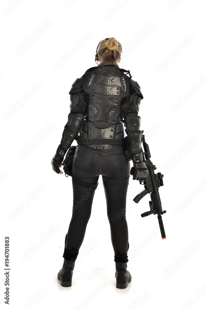 full length portrait of female  soldier wearing black  tactical armour, standing  with back to the camera holding a gun, isolated on white studio background.