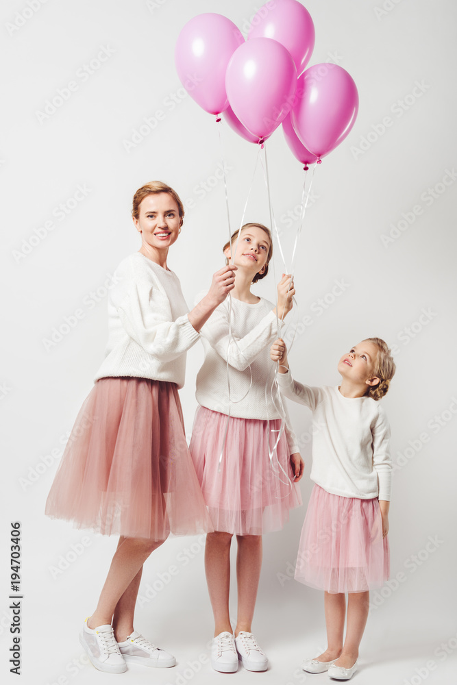 smiling mother and daughter in similar clothing with pink balloons isolated on grey smiling mother and daughter in similar clothing with pink balloons isolated on grey
