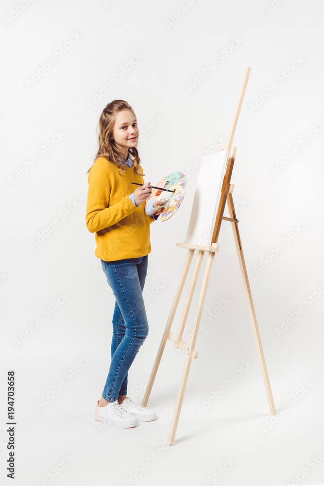 teen female painter with paint brush and palette near easel with blank canvas on white teen female painter with paint brush and palette near easel with blank canvas on white