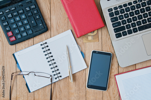 Closeup open notebook, laptop, calculator, pen, smartphone on a wooden table. Business concept