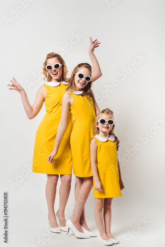 happy mother and daughters in similar retro style yellow dresses on white