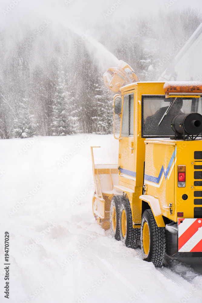 Big yellow snowplough with screw and helix is cleaning the road while a powerful stream of white snow go out Big yellow snowplough with screw and helix is cleaning the road while a powerful stream of white snow go out